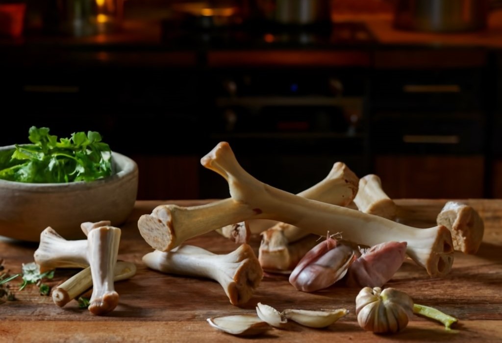 A rustic kitchen setting with an array of soup bones (beef, chicken, pork) laid out on a wooden cutting board, highlighting their raw beauty and variety.